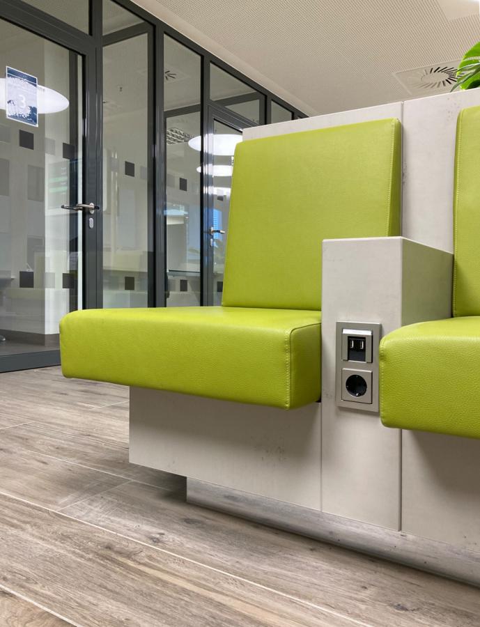 Sitzmöbel in Betonoptik mit grünen Polstern und integrierter Medientechnik