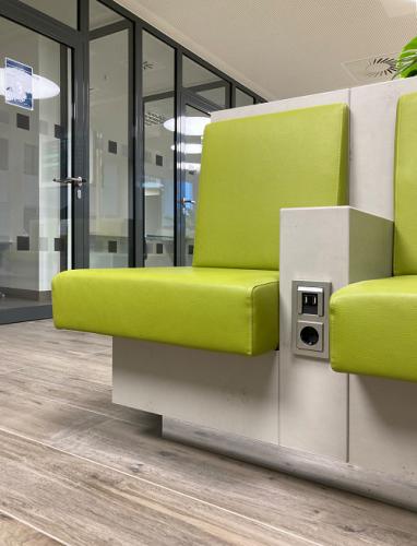 Sitzmöbel in Betonoptik mit grünen Polstern und integrierter Medientechnik