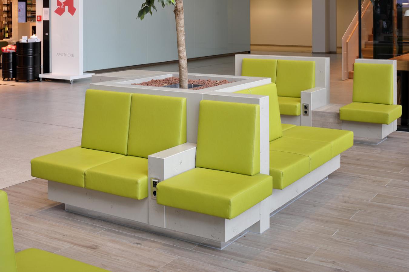 Sitzmöbel in Betonoptik mit grünen Polstern und integrierter Medientechnik