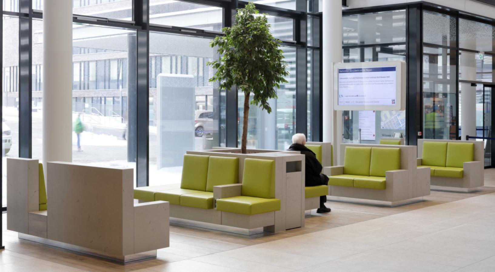 Sitzmöbel in Betonoptik mit grünen Polstern und integrierter Medientechnik im Wartebereich eines Krankenhauses